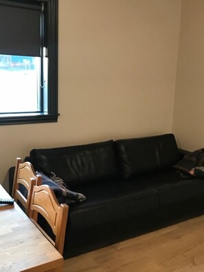 A room with a black leather sofa, a wooden chair, and a table.