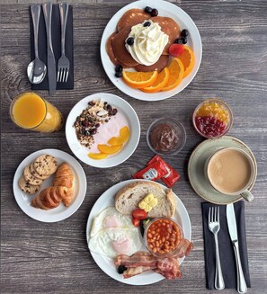 A breakfast spread with pancakes, eggs, bacon, toast, and various fruits and spreads.
