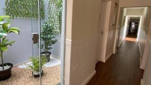 A corridor with a glass door leading to a small garden area with potted plants and a wooden floor. - Hotel Colonial (Porto Ferreira)