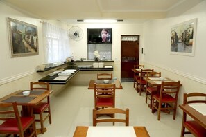 Una zona de dinar amb taules i caires de fusta, un televisor penjat a la paret i obres d'art a les parets.