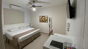 A hotel room with a bed, a desk with a computer, a television, and a ceiling fan. - Hotel Colonial (Porto Ferreira)