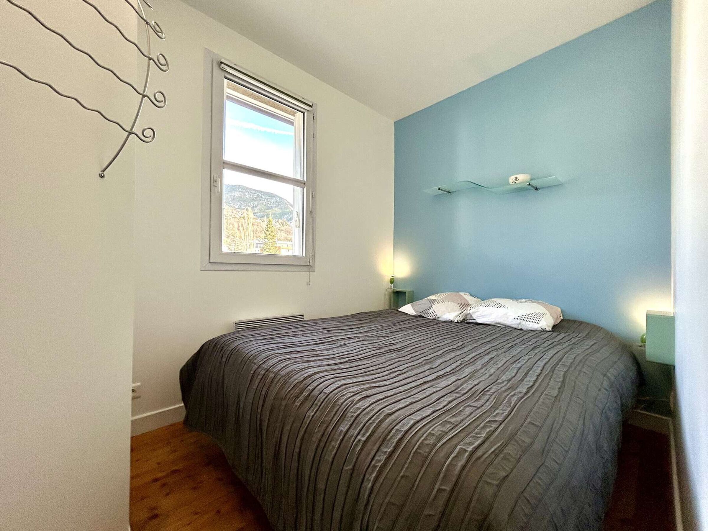 Une chambre à coucher avec un lit, une fenêtre et un luminaire fixé au mur.