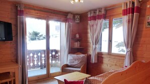 A cozy room with wooden walls and a balcony. It includes a sofa, a small table, and a chair.