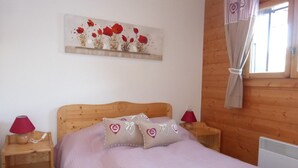 A bedroom with a wooden headboard, a bed with a light-colored bedspread, two bedside tables with lamps, and a wall-mounted shelf with decorative items.