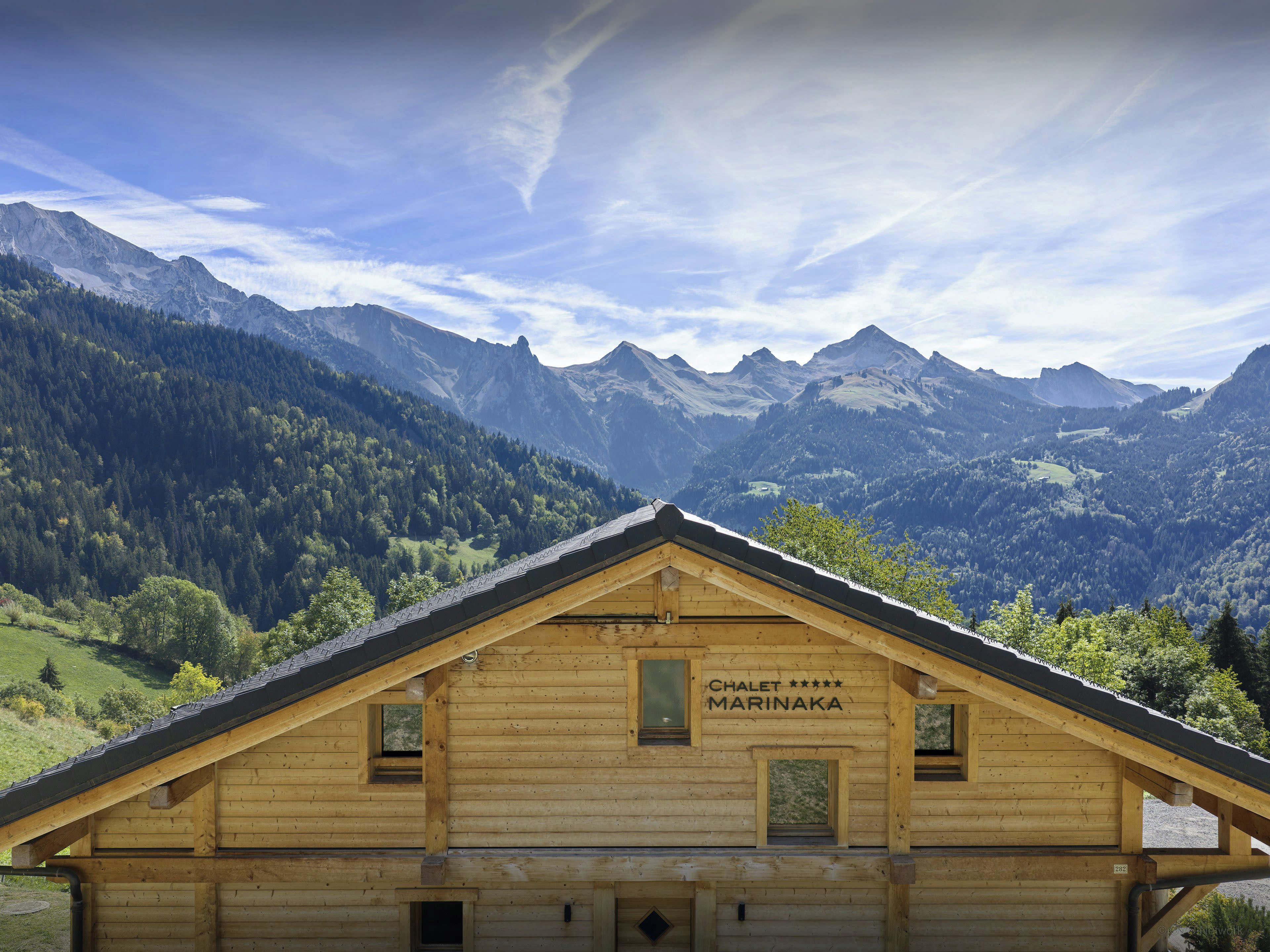 A wooden chalet with a sign reading 'Chalet Marinka' amidst a mountainous landscape.