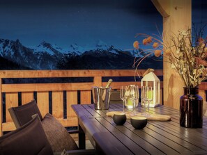 Une terrasse en bois avec une table dressée pour le repas, un vase rempli de fleurs et une vue sur les montagnes en arrière-plan.
