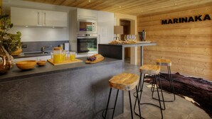 Una cocina moderna con techo de madera, horno empotrado y una zona de bar con taburetes.
