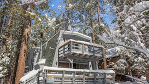 Una cabaña nevada con balcón, rodeada de árboles.
