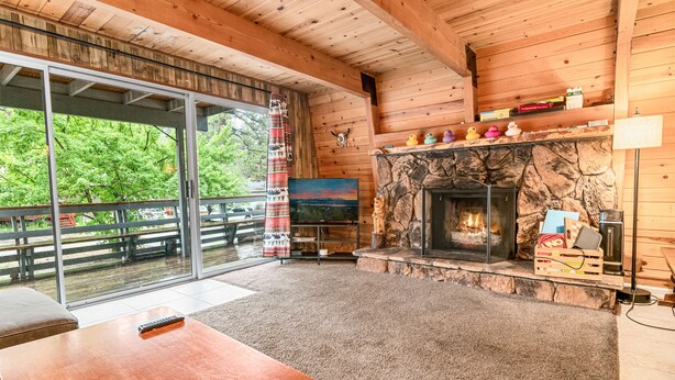 Interior acogedor de una cabaña con chimenea de piedra, televisor y un gran ventanal corredera que da a una terraza.