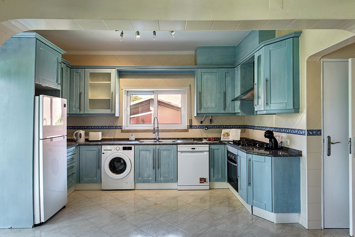 A compact kitchen with teal cabinets, a washing machine, and a dishwasher.