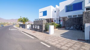 Un edificio moderno con fachada blanca y detalles azules, un pavimento y una carretera despejada con un coche a lo lejos.