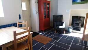 A room with a wooden table and chairs, a red cabinet, a patterned chair, and a fireplace. - Harbor View Cottage (Coomnahincha, Cahersiveen)