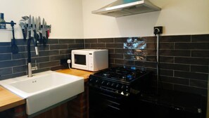 A kitchen with a white sink, a microwave, a stove, and a backsplash of dark tiles. - Harbor View Cottage (Coomnahincha, Cahersiveen)