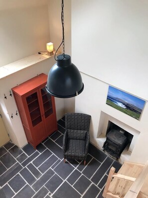 A room with a black pendant lamp, a red cabinet, a patterned armchair, a fireplace, and a tiled floor.