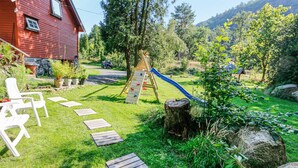Ein Garten mit einer Holzspielstruktur, einem roten Haus und einem Pfad zu einem weißen Stuhl.