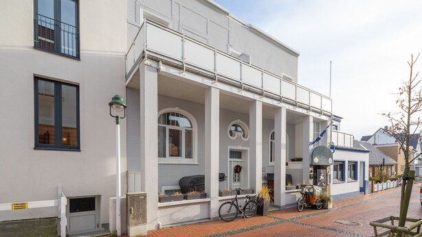 A white building with a covered porch, a bicycle, and a tricycle parked outside. - FeWo shooting star, downtown, central location, (Norderney)