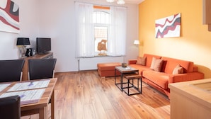 A modern living room with a wooden floor, a sofa, a coffee table, and a TV. - FeWo shooting star, downtown, central location, (Norderney)