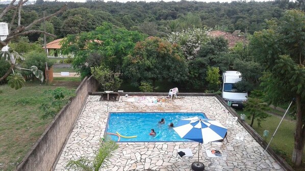 Una piscina con piastrelle in pietra, circondata da un muro in pietra, con alcune persone che nuotano e un ombrellone da spiaggia.