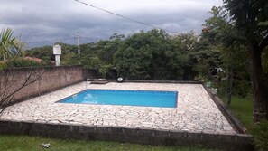 Una piscina con bordo in pietra, circondata da un basso muro in mattoni e vegetazione rigogliosa.