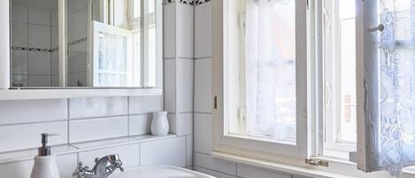 Une salle de bain avec un lavabo blanc, un miroir et une fenêtre ornée de rideaux en dentelle.