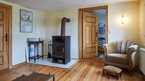 A cozy living room with a wood-burning stove, a comfortable armchair, and a small table with books. - Charming farmhouse (Rheinsberg, OT Linow)