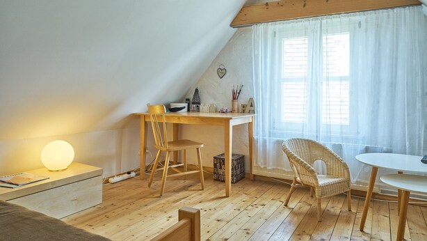 A cozy attic room with a wooden desk, two chairs, a small table, and a window with sheer curtains. - Charming farmhouse (Rheinsberg, OT Linow)