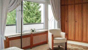 Un dormitorio con una ventana grande, un armario de madera, una silla y una cama.