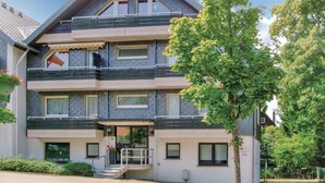 Un edificio residencial de varios pisos con un balcón en el segundo nivel, un pequeño porche con escalones y un árbol en la fachada.