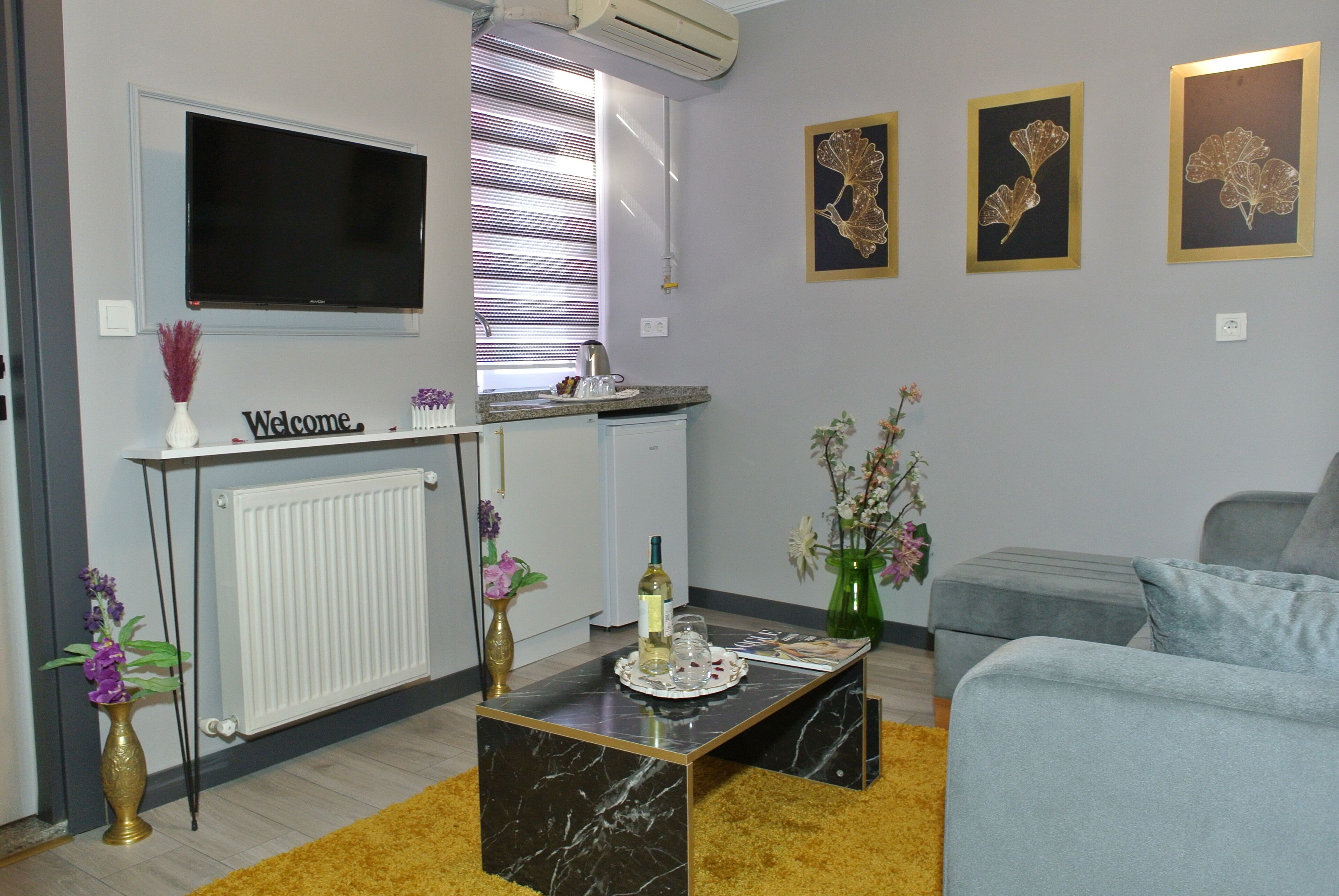 Una sala de estar con televisor, mesa de centro, sofá y una cocina con ventana.