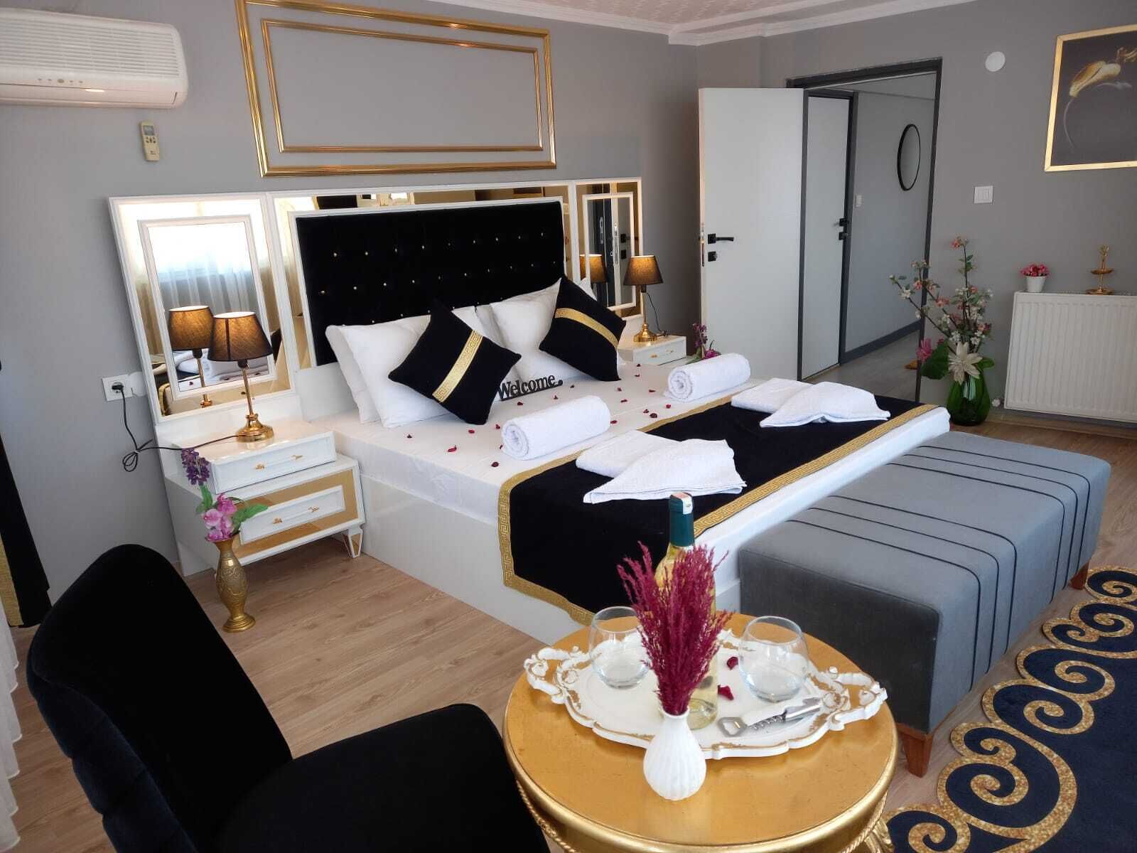 A hotel room with a bed, bedside tables, a desk, a chair, a round table with a vase, and a door.