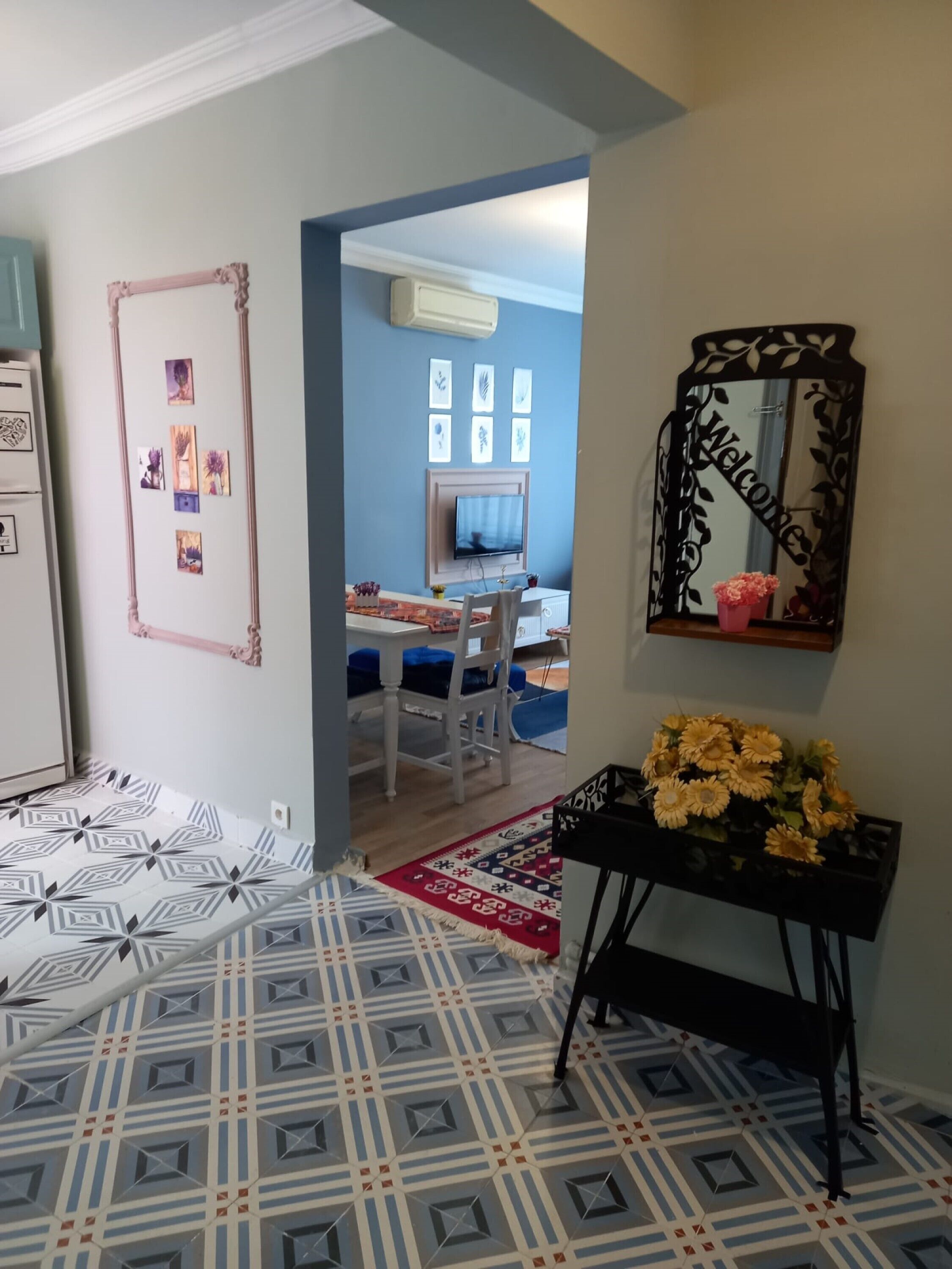 Ein Zimmer mit einem gemusterten Boden, einem Schreibtisch mit Stuhl, einem Fernseher, einem Spiegel und einer Vase mit Blumen.