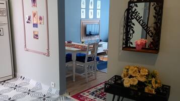 Ein Zimmer mit einem gemusterten Boden, einem Schreibtisch mit Stuhl, einem Fernseher, einem Spiegel und einer Vase mit Blumen.