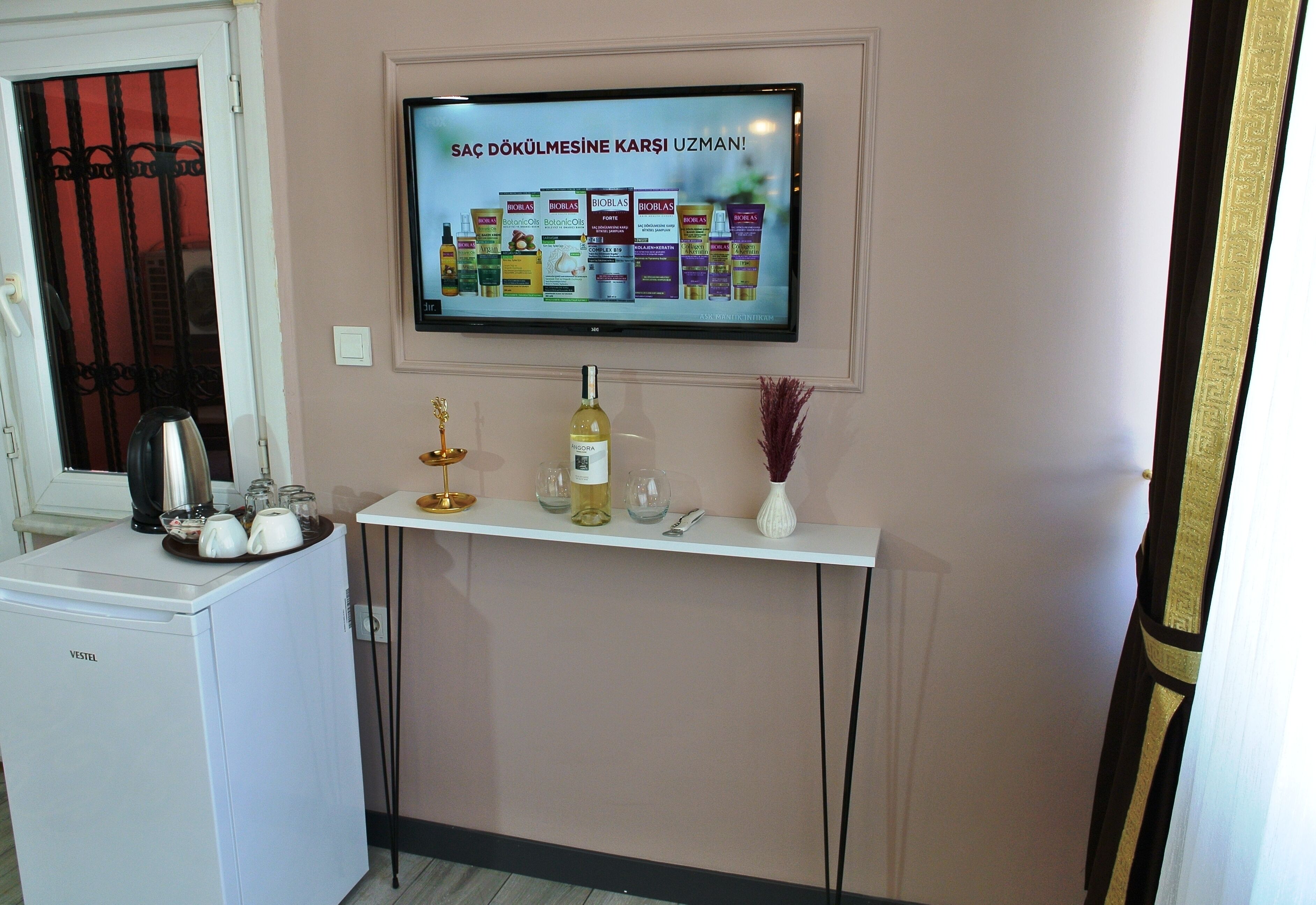 A kitchenette with a white refrigerator, a small sink, and a countertop with a bottle of olive oil, a glass, and a vase.