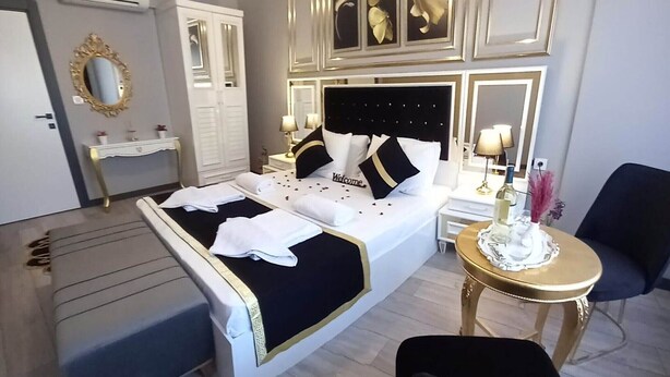 A hotel room with a bed, bedside tables, a vanity with a mirror, a chair, and a small round table with a lamp. - Emirhan Guest House & Suites (Istanbul)