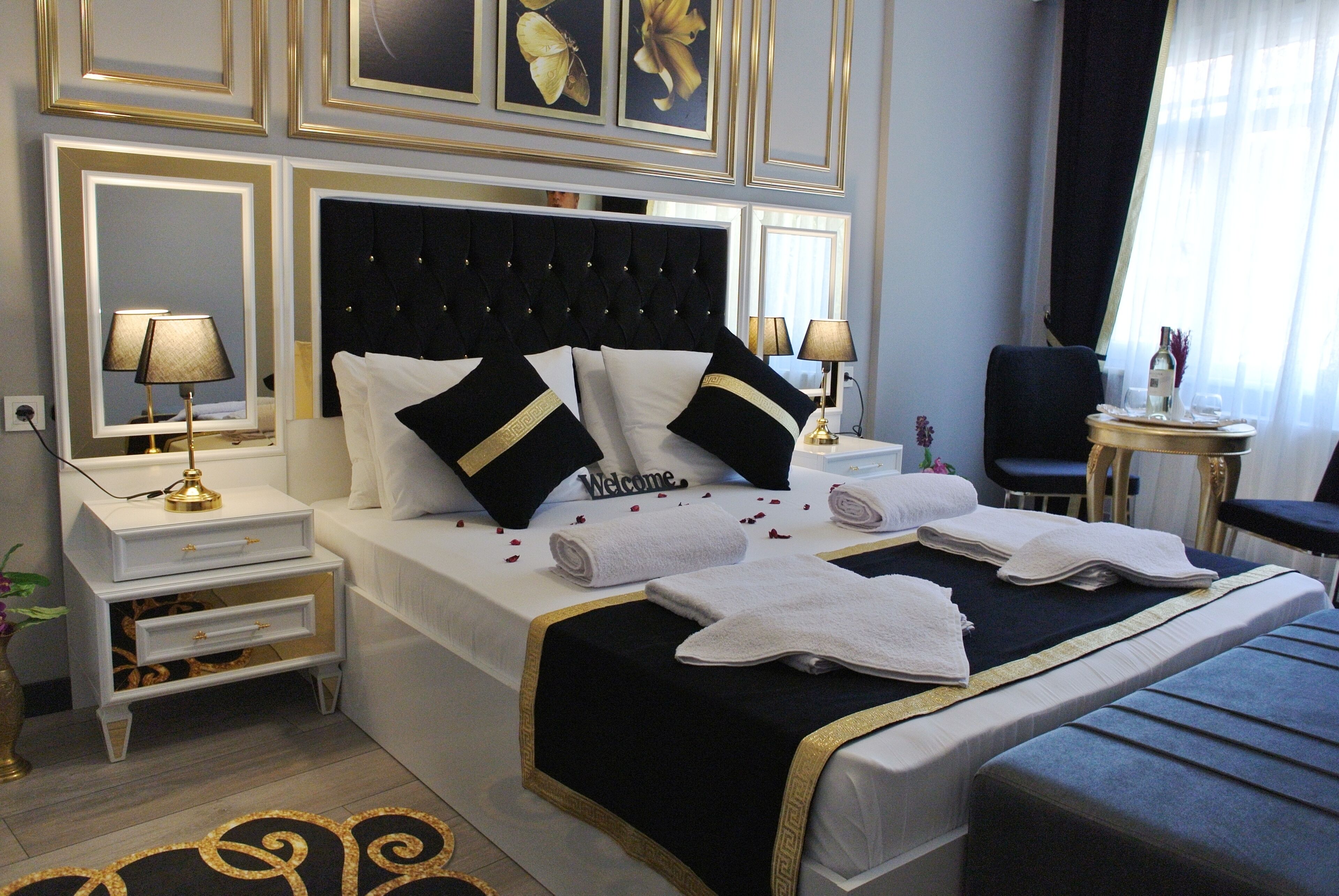 A hotel room with a neatly made bed, a bedside table with a lamp, a chair, and a small table with a bottle and glasses.