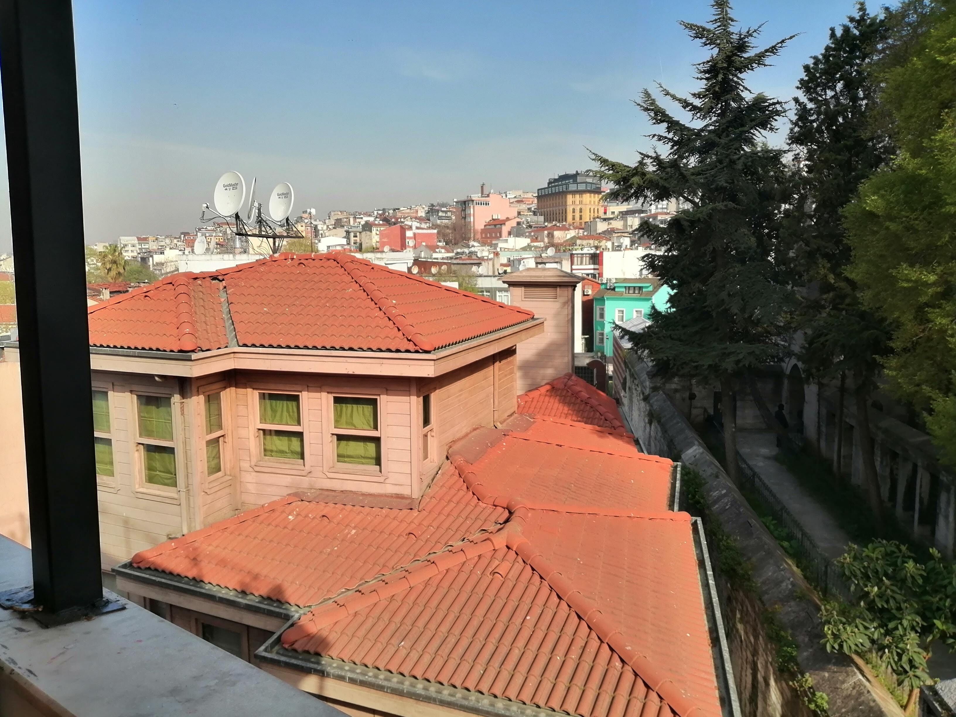Vista de un paisaje urbano con edificios, antenas parabólicas y un muro de piedra con vegetación.