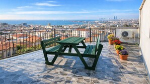 A balcony with a stone-tiled floor, two green benches, and potted plants. - Emirhan Guest House & Suites (Istanbul)