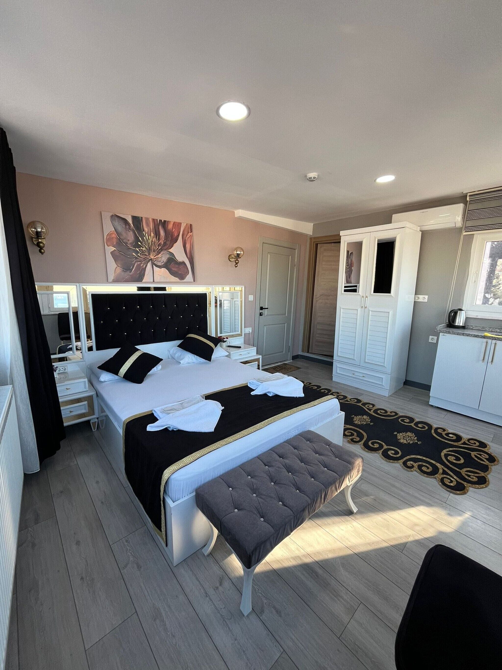 A bedroom with a bed, bedside tables, a bench, a painting, a wardrobe, and a bathroom.