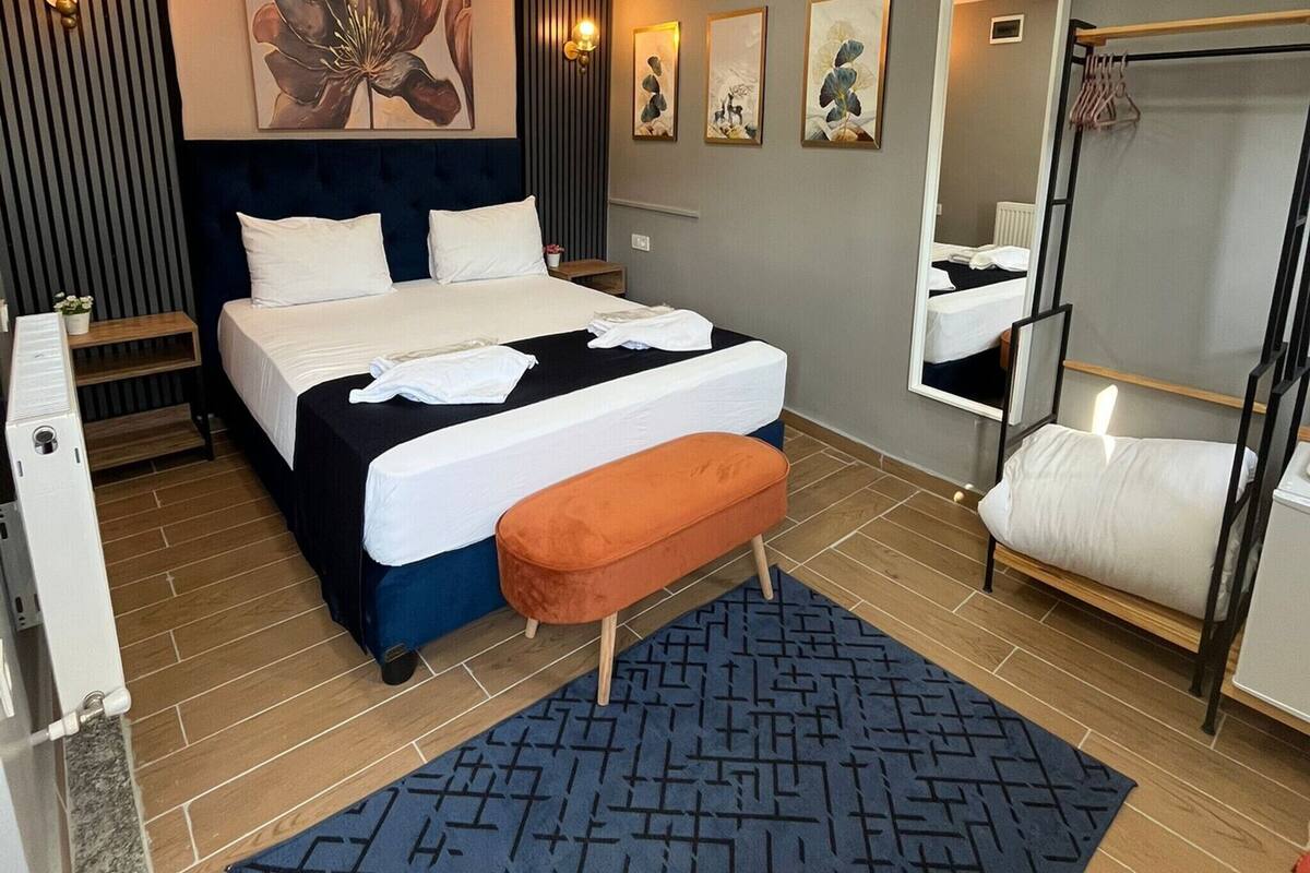 A hotel room with a bed, a bench, a mirror, a radiator, and artwork on the walls.