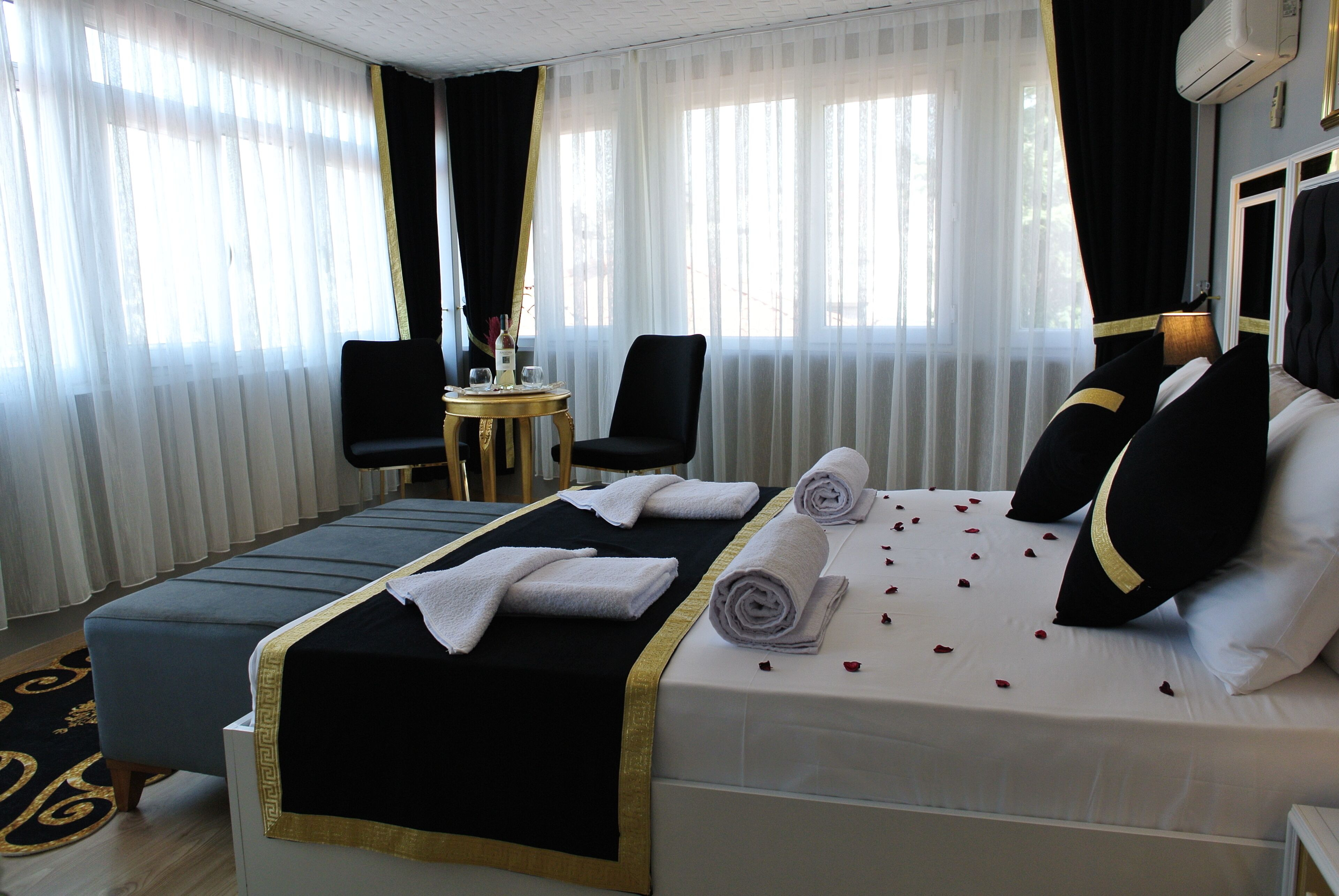 A hotel room with a large bed, a small round table with a chair, and a window with sheer curtains.