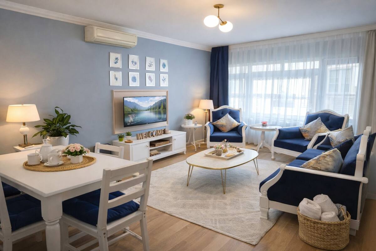 A modern living room with a sofa set, a dining table with chairs, a coffee table, a TV, and a 'WELCOME' sign on the wall.