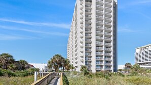A tall, multi-story hotel with balconies, located near a beach with palm trees and a boardwalk. - Ocean view condo, fully renovated + Free Attraction Tickets! (Myrtle Beach)