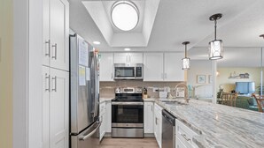 A modern kitchen with stainless steel appliances, white cabinetry, and a marble countertop. - Ocean view condo, fully renovated + Free Attraction Tickets! (Myrtle Beach)