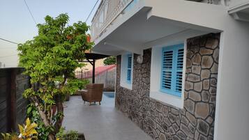 A covered outdoor area with a stone wall, a wicker chair, and a potted plant.