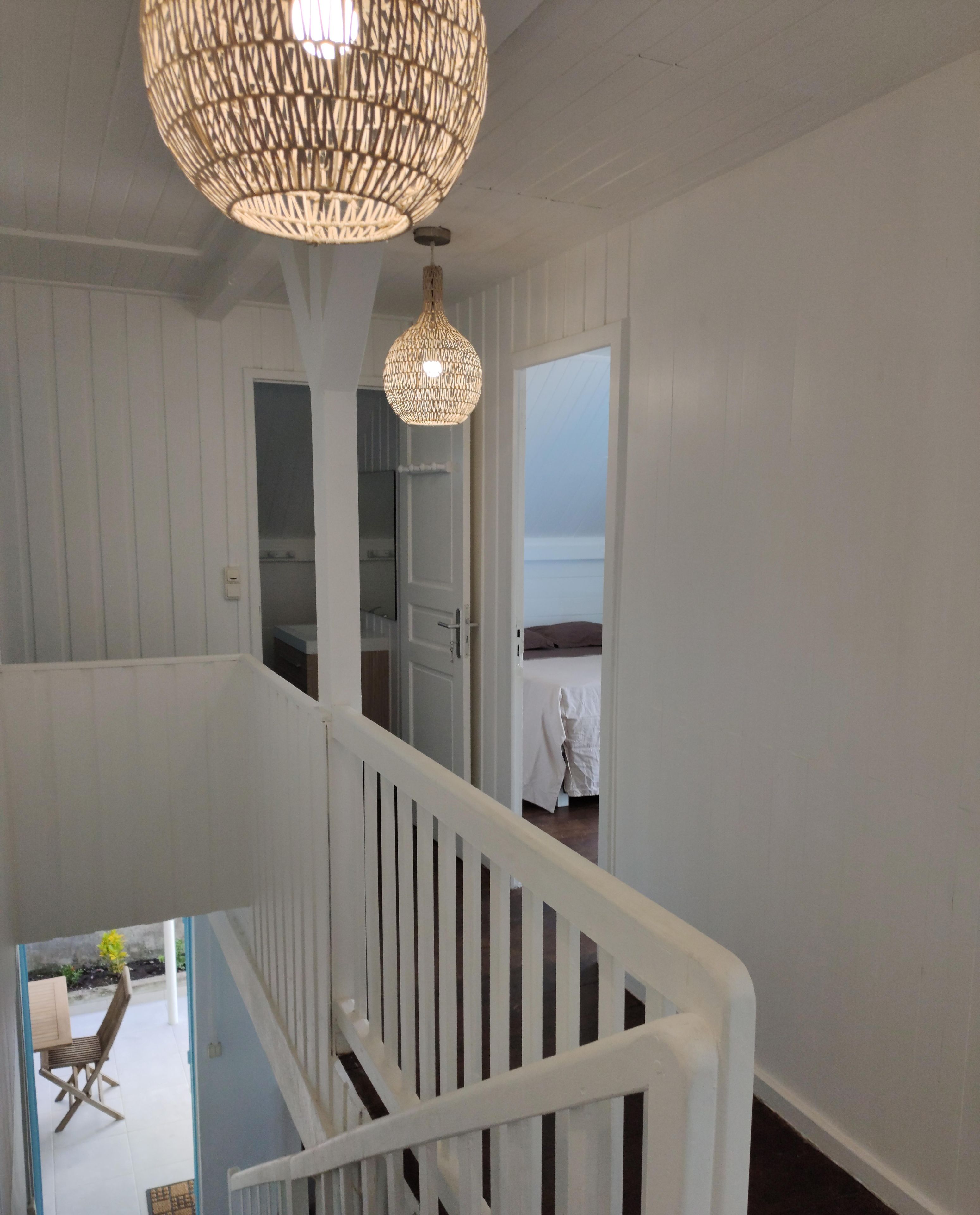 A staircase with white railings leading to a room with a bed and a hanging light fixture.