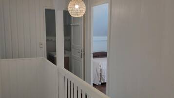 A staircase with white railings leading to a room with a bed and a hanging light fixture.