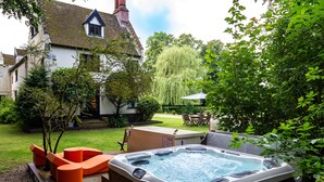 Un jacuzzi en un patio trasero con una casa, muebles de jardín y un árbol.