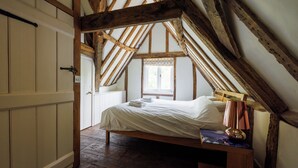 Un dormitorio con techo inclinado, vigas de madera, una cama con ropa blanca y un ventanal con vistas al exterior.