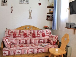 A cozy living room with a wooden sofa covered in red and white patterned fabric, a wooden chair, and a small table with a candle. - Studio for 4 near shops and slopes in Risoul (Risoul)