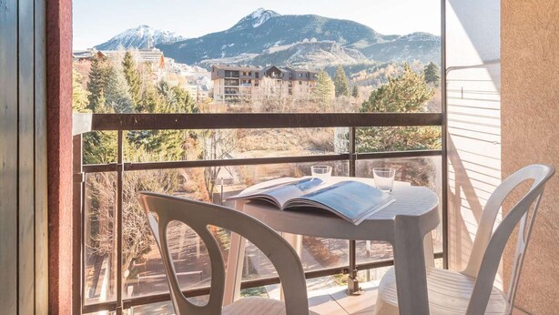 A balcony with a table and chairs, overlooking a mountainous landscape with buildings.
